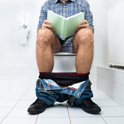 Mann sitzt auf der Toilette und liest ein Buch 