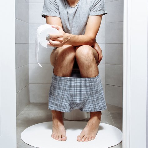 Mann sitzt im Schlafanzug auf einer Toilette.