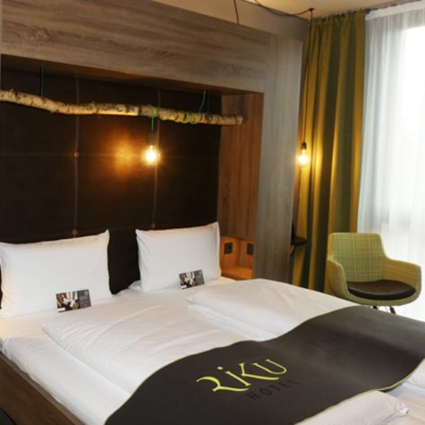 Doppelbett im RiKu Hotelzimmer mit Stuhl und Lampen.