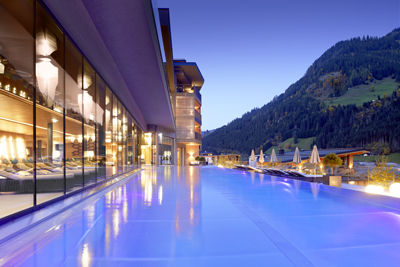Liegen im abgetrennten Spa-Bereich und das Sportbecken im malerischen Bergpanorama während des Sonnenuntergangs. © DAS EDELWEISS Salzburg Mountain Resort, Fotograf Michael Huber