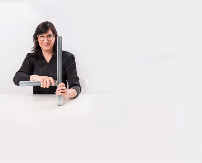 Designerin Tilla Goldberg sitzend an einem weißen Tisch und mit zwei Metallstangen in der Hand.