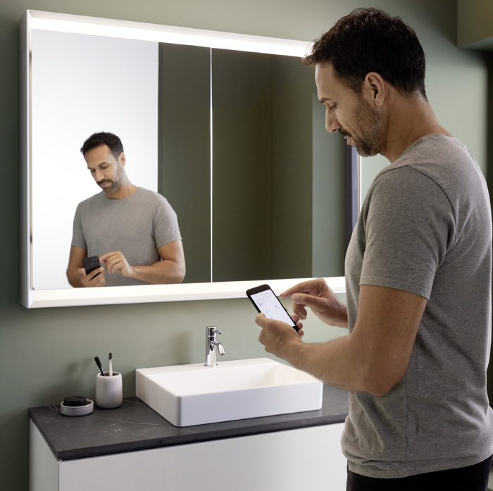 Mann mit Handy im Badezimmer vor Geberit ONE Lichtspiegelschrank